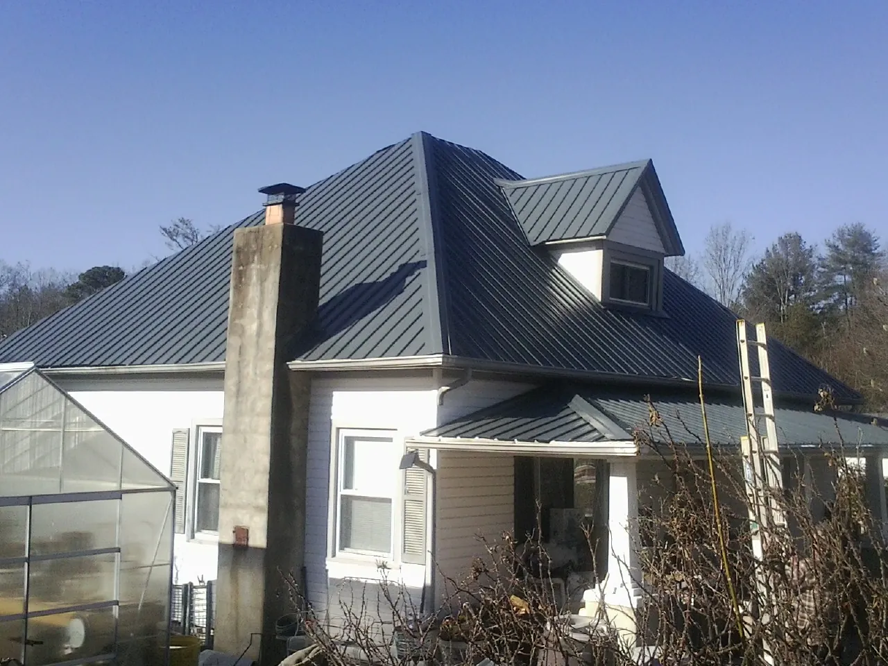 Dark blue standing seam metal roof on a white farmhouse with dormer — Slate & Tile Roof Repair by Roofing Brothers in Stow
