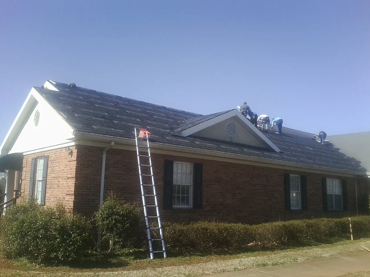Crew tearing shingles off a brick ranch roof with a ladder set — Emergency Roof Repair work by our crew in Stow
