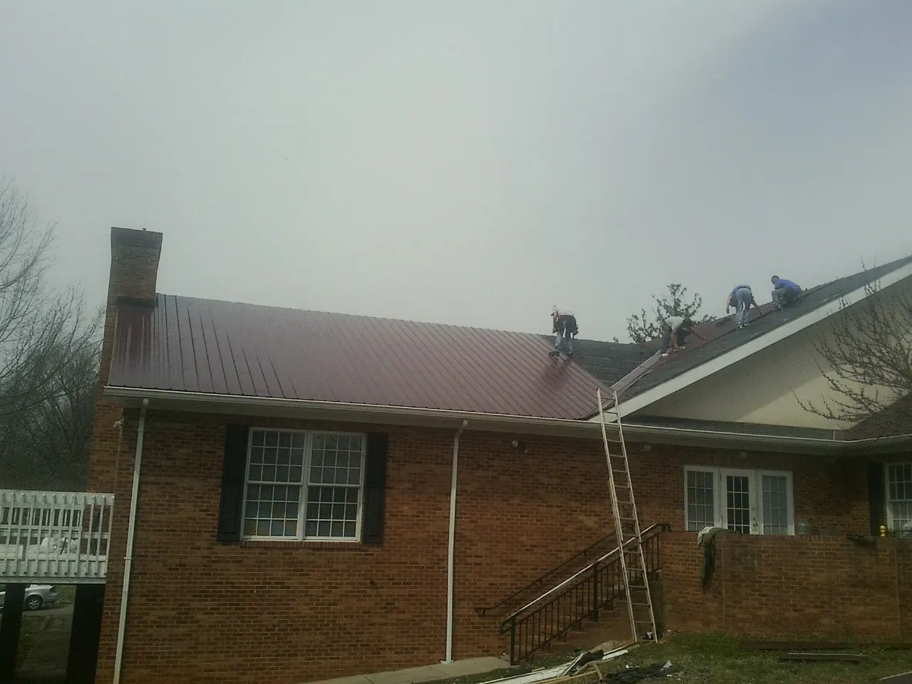 Crew setting red metal roofing panels on a brick home in Stow